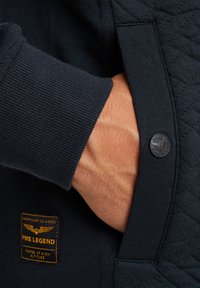 Dunkelblaues Sweatshirt mit gerippten Bündchen, gestepptem Material am Körper und einem Patch mit "PME Legend"-Markenlogo.