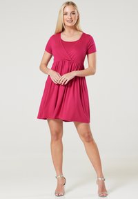 Short-sleeved dress in bright pink fabric with a fitted bodice, gathered skirt, and a V-neckline, paired with metallic strappy heels.