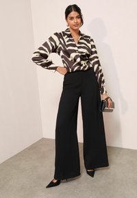 Nupitudega pluus musta ja kreemja zebra mustriga, koos kõrge vöökohtadega mustade laia jalgadega pükste ja mustade terava nina kontsadega.