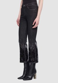Jeans in denim nero con dettagli in paillettes ai polsini, caratterizzati da un design aderente e leggermente svasato. Abbinati a stivaletti neri alla caviglia.