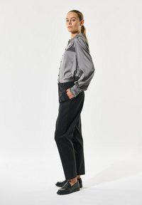 Graue Satinbluse mit Knopfdetails, kombiniert mit schwarzen, taillierten Hosen und schwarzen Slippern, zeigt ein schlankes, elegantes Design.