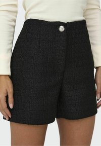 Schwarze strukturierte Shorts mit hoher Taille und einer einzelnen silbernen Knopfverschlüssen vorne. Der Stoff hat ein gewebtes Aussehen.