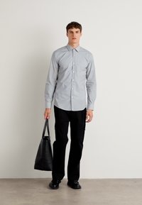 Lyseblå og hvite striperert skjorte med knapper, svarte bukser og en svart totebag. Skjorten har en klassisk krage og knapper foran.