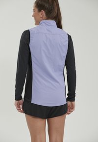 Korte mouwen sporttop met een lavendelkleurige achterkant, zwarte mouwen en zijpanelen; gladde textuur met contrasterende stikseldetails.