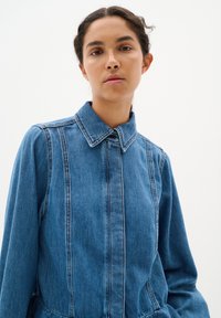 Sininen farkk Shirt, joka on varustettu kauluksella, pitkillä hihoilla ja pystysaumoilla. Pehmeä rakenne, jossa on istuva vyötärö ja levenevät yksityiskohdat.