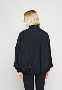 Črna lahka jakna z visokim ovratnikom, elastičnimi manšetami in pasom. Ima teksturirano površino in oversized kroj.