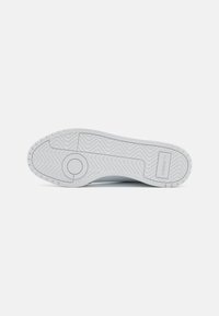Hvid gummisål til sneakers med teksturerede mønstre, der har bølgende linjer og cirkulære accenter. Logo trykt på siden.