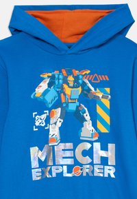 Modra bombažna kapuca z oranžno podloga, ki prikazuje grafiko mehaniziranega robota in besedilo "MECH EXPLORER" v metalno srebrni barvi.