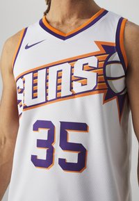 Maillot de basket-ball blanc avec "SUNS" en lettres violettes en gras, accents orange, et le numéro "35" en violet. Tissu en maille texturée, design sportif.