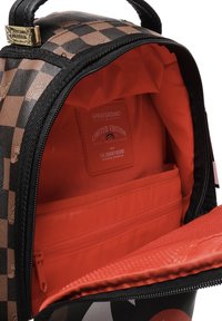 Mochila con diseño de tablero de ajedrez en marrón y negro, con un interior rojo brillante y un bolsillo con cremallera para organización.