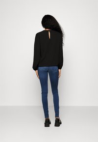 Black long-sleeve top with a keyhole back detail, paired with blue skinny jeans and black chunky shoes, viewed from the back.