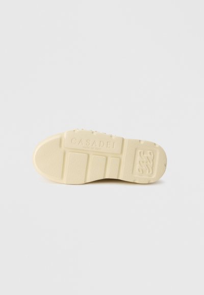 Σόλα αθλητικού παπουτσιού σε κρεμ απόχρωση με υφή που περιλαμβάνει αυλακώσεις, εγγραφή λογότυπου και ομαλή στρογγυλεμένη μύτη.