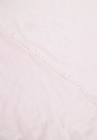 Tissu rose pâle doux avec une couture diagonale ornée de fines franges délicates traversant le centre.