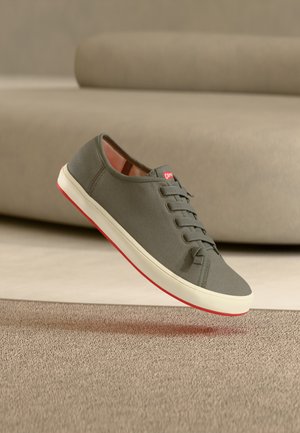 Grauer Sneaker aus Stoff mit strukturierter Oberseite, weißer Zwischensohle und roter Außensohle, ausgestattet mit sechs Ösen und einem Logo in der Nähe der Schnürsenkel.