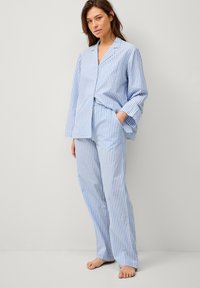 Blauw-wit gestreept pyjama-set, met een knoopsluiting blouse met lange mouwen en een borstzak, en losse bijpassende broeken.