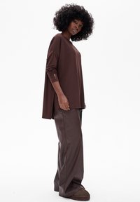 Bruine oversized lange mouwen top met zijopeningen, gecombineerd met bruine wijde pijpen. Zachte stof, ontspannen pasvorm en minimalistisch ontwerp.