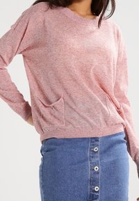 Rosa melerat stickad tröja med rundad halsringning, långa ärmar och en framlappficka, kombinerad med en blå denimkjol med knappdetaljer.