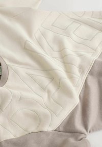 Light-colored sweatshirt featuring a large graphic in a contrasting shade, with a soft, textured finish and rounded neckline.