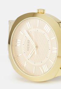 Gold watch with a textured, light-colored dial featuring Roman numerals and gold hands. Includes a crown and a polished case.