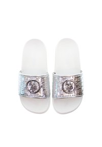 Vita glid sandaler i vitt med ett silverfärgat texturerat rem som har ett emblem. Remmen har ett geometriskt mönster och en central medaljdetalj.