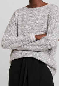 Gray textured sweater with a boat neckline and stripes at the cuffs. Loose fit with dropped shoulders. Paired with black trousers.