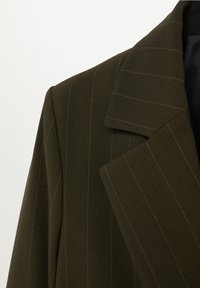 Blazer vert olive foncé à fines rayures avec un large revers à encoche, couture d'épaule visible et doublure intérieure noire.