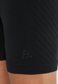 Close-up of a person’s thigh wearing black textured athletic shorts with a subtle stamped logo on the lower side.