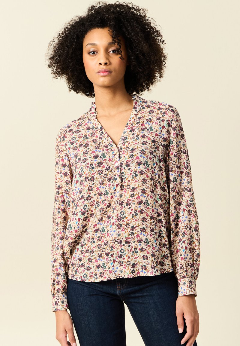 Blumenbluse mit langen Ärmeln in Pastelltönen, mit einem gespaltenen Ausschnitt und gerafften Manschetten. Hergestellt aus leichtem, strukturiertem Stoff.