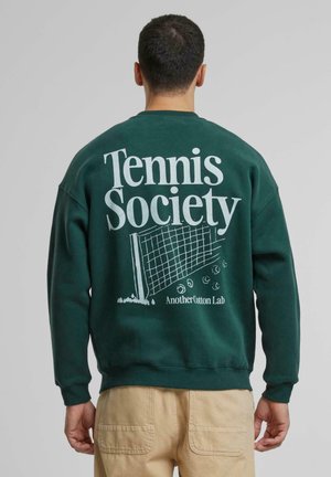 Dark green sweatshirt featuring the text "Tennis Society" and a tennis net graphic on the back. Soft texture and relaxed fit.