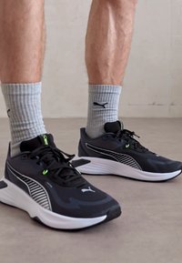 Pantofi sport negri cu accente albe și detalii verzi, având un material texturat și un design cu dungi. Purtați cu �șosete gri cu dungi.