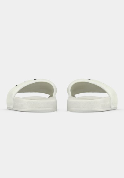 Sandales à glissière blanches avec une tige texturée, design ouvert à l'arrière et semelle plate. Style minimaliste avec des accents noirs contrastants.