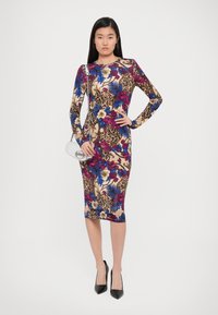Bloemen bodycon jurk met lange mouwen; bevat meerkleurige bloemen- en luipaardprintpatronen. Gepaard met een zilveren clutch en zwarte hakken.
