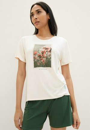 Witte t-shirt met een bloemenprint van roze papavers op een groene achtergrond, gecombineerd met donkergroene shorts. Zacht materiaal, korte mouwen en ronde hals.