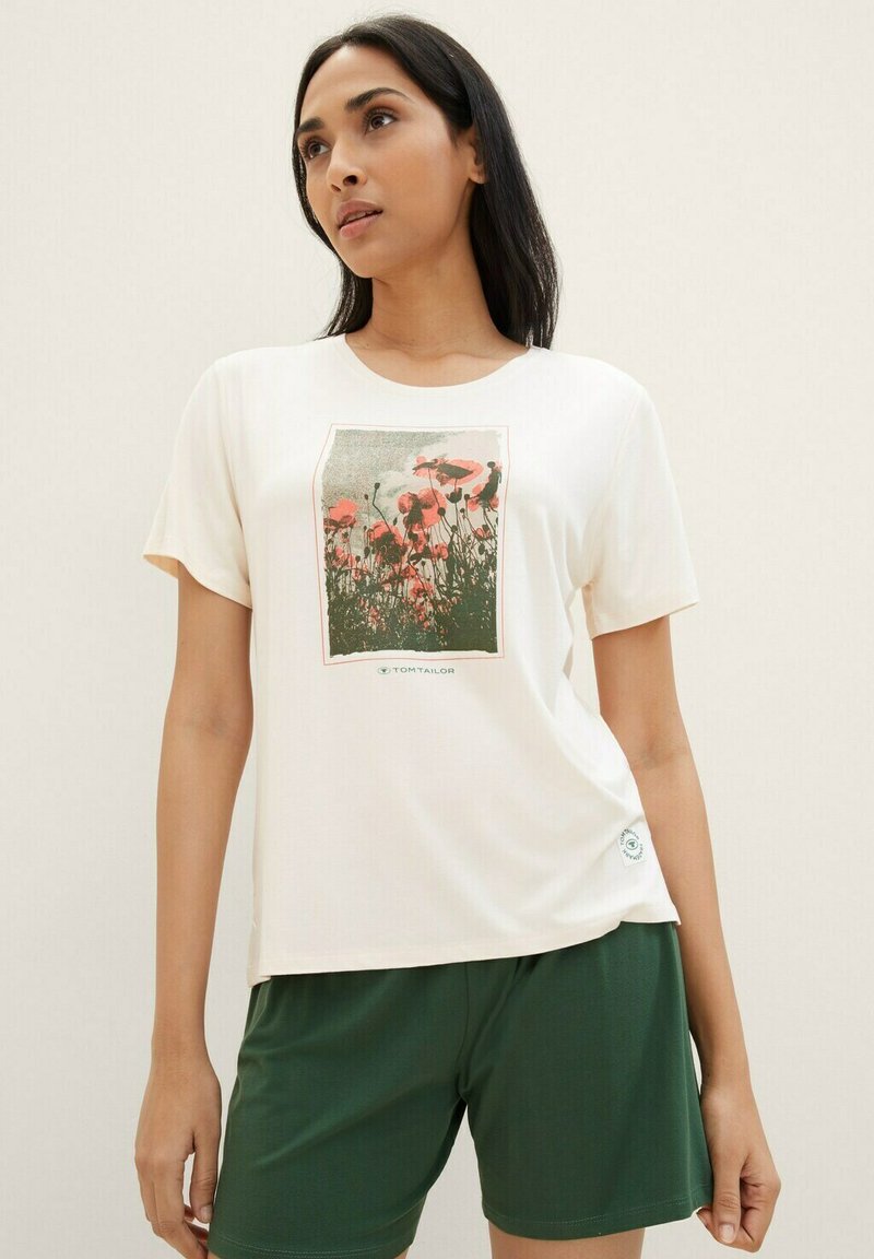 Witte t-shirt met een bloemenprint van roze papavers op een groene achtergrond, gecombineerd met donkergroene shorts. Zacht materiaal, korte mouwen en ronde hals.