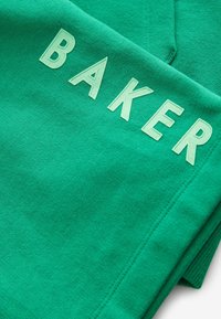 Vihreä collegepaita, jossa on sana "BAKER" kohotetulla vaaleanvihreällä kirjainpainatuksella. Kankaan pinta on pehmeä ja siinä on ommellut saumat.