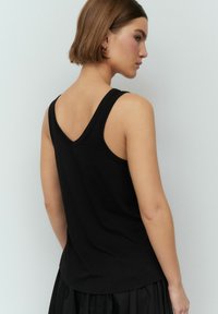 Zwarte mouwloze top met een V-vormige achterkant. Gemaakt van zacht materiaal, heeft het een getailleerde silhouet en een gladde textuur. Geen opvallende accenten.
