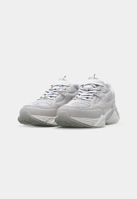 Gray athletic shoes with mesh and suede materials, rounded toe, flat rubber sole, and contrasting dark laces. "Fila" logo on side.