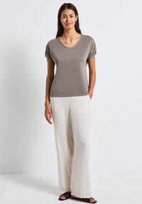 Haut gris à manches courtes avec un col plongeant, associé à un pantalon en lin ample de couleur blanc cassé et des sandales noires. Texture de tissu lisse.