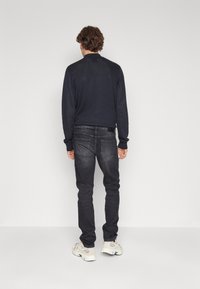 Suéter azul marino oscuro combinado con jeans gris oscuro. Los jeans tienen bolsillos traseros con costuras sutiles. El calzado incluye zapatillas gris claro.