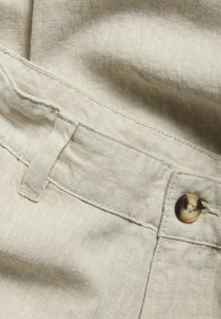 Lys beige linned stof med en synlig tekstur, med en frontknaplukning og stiktet taljedetalje.