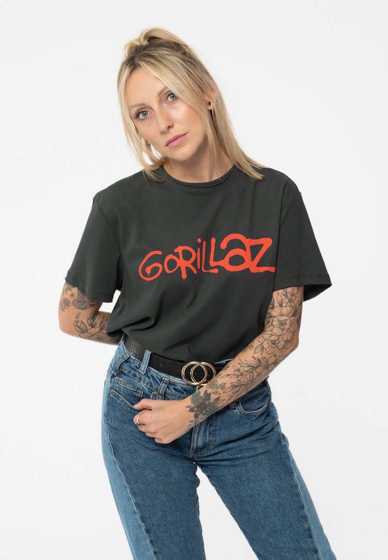 Black short-sleeve t-shirt with red "Gorillaz" graphic, paired with light blue high-waisted jeans and a black belt with circular accents.