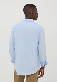 Camicia a maniche lunghe azzurro chiaro con colletto a punta e polsini abbottonati. Tessuto morbido, taglio dritto e una leggera coda sul retro.