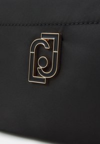 Surface texturée noire avec un accent de logo abstrait en ton doré. Le design présente une forme distinctive et des finitions lisses.