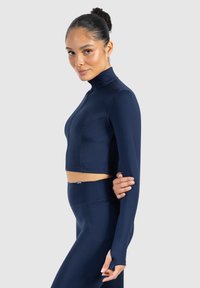 Marineblauw, cropped sporttop met hoge kraag, lange mouwen en aansluitend ontwerp. Beschikt over een soepele, stretchy stof en subtiele naadtoeslagen.