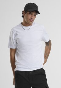 T-shirt en coton blanc à manches courtes, col rond et texture lisse, associé à une casquette noire avec œillets.