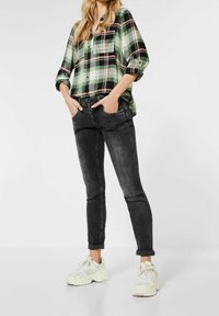 Grön och svart rutig skjorta med knappar och uppvikta ärmar, kombinerad med svarta skinny jeans och vita sneakers. Avslappnad, modern passform.