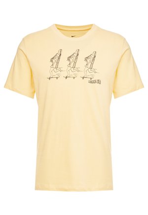 Żółta bawełniana koszulka z nadrukiem przedstawiającym trzy biegnące postacie w dużych butach. Logo „Nike SB” umieszczone w prawym dolnym rogu.