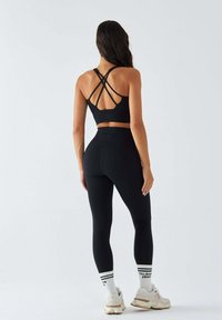 Czarny sportowy krótki top z krzyżującymi się ramiączkami oraz czarne legginsy z wysokim stanem. Do tego białe sneakersy z beżowymi akcentami i skarpetki w paski.