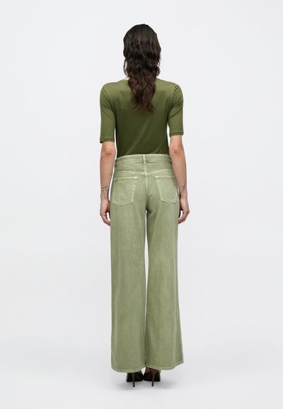 Εφαρμοστή μπλούζα σε ελιά πράσινο χρώμα, συνδυασμένη με ψηλόμεσο, φαρδύ παντελόνι σε ανοιχτό πράσινο χρώμα, με πίσω τσέπες και υφή υφάσματος.