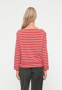 Rød og hvit stripete langermet skjorte med bred utringning og avslappet passform. Stoffet ser mykt ut, med synlig søm i nederkant og mansjetter.